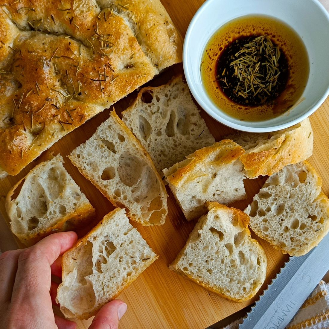 Rosemary focaccia sliced on a wooden board with a bowl of olive oil and balsamic